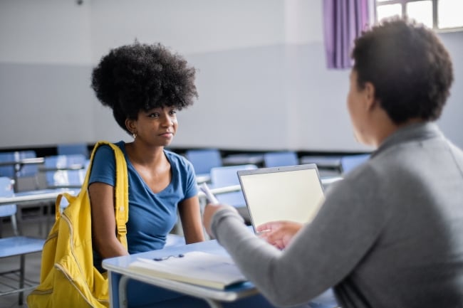 Student consulting teacher in classroom setting