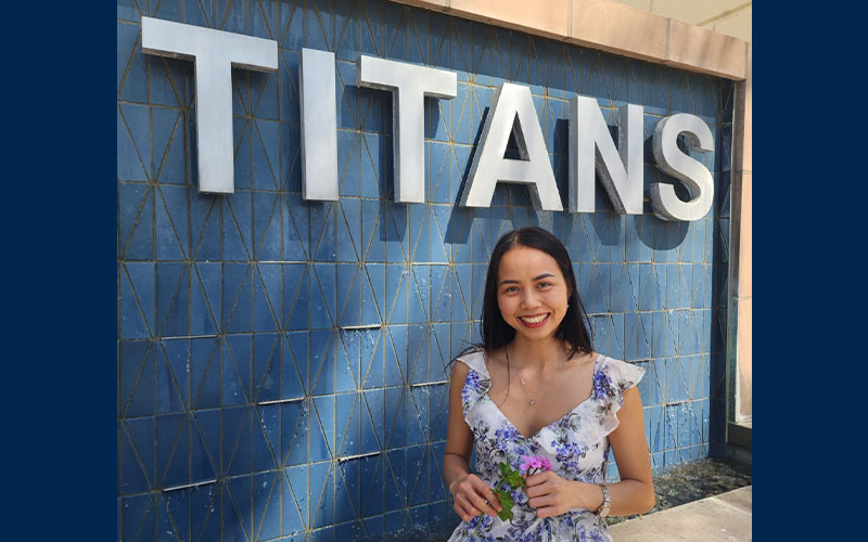 Woman smiling in front of 'TITANS' sign on blue wall